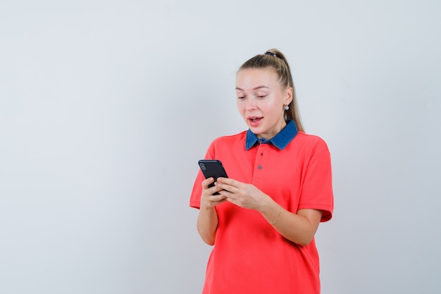 Mujer joven con teléfono móvil en camiseta y mirando feliz. vista frontal.