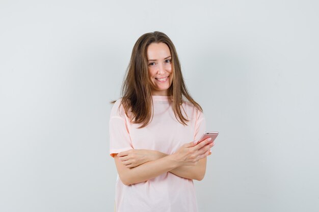 Mujer joven con teléfono móvil en camiseta rosa y mirando alegre. vista frontal.