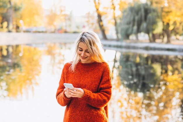 Mujer joven con teléfono en el parque junto al lago