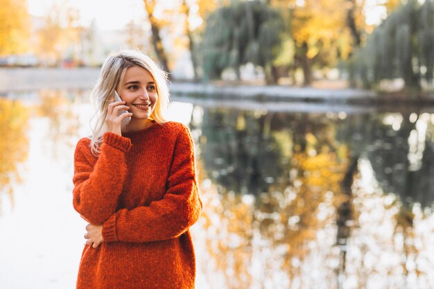 Mujer joven con teléfono en el parque junto al lago