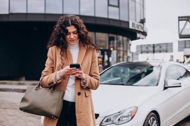 Mujer joven con teléfono y de pie junto al coche