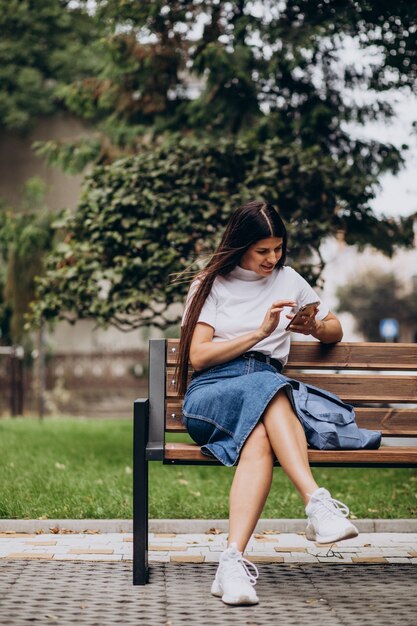 Mujer joven con teléfono y sentado en un banco en el parque