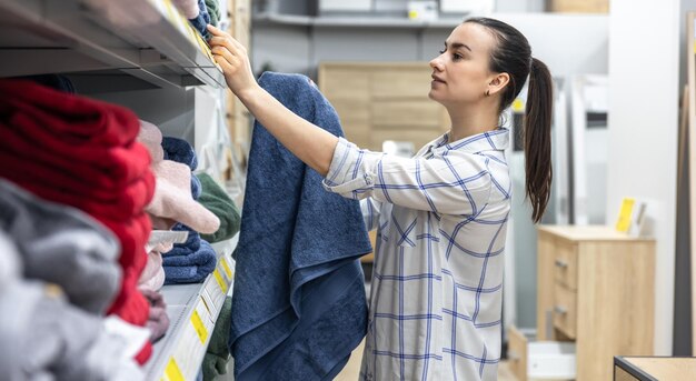 Una mujer joven en una tienda de artículos para el hogar elige una toalla de baño azul