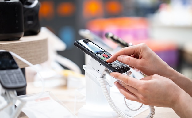 Una mujer joven en la tienda está de pie cerca del stand y elige un teléfono