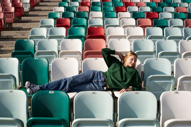 Foto gratuita mujer joven de tiro completo sentada en las tribunas