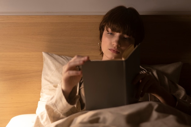 Mujer joven de tiro medio leyendo en la cama