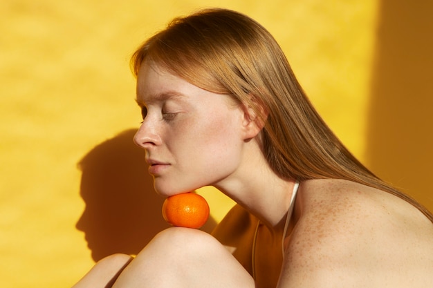 Mujer joven de tiro medio posando con mandarina