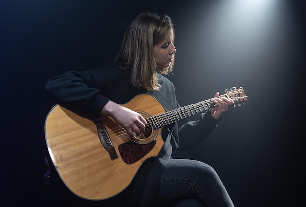 Mujer joven tocando la guitarra acústica en una habitación oscura con neblina