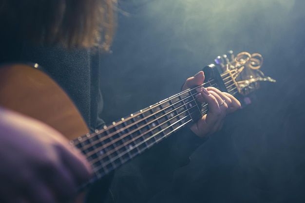 Mujer joven tocando la guitarra acústica en una habitación oscura con neblina