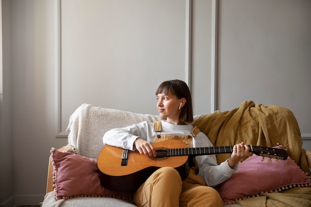 Foto gratuita mujer joven tocando la guitarra en interiores con espacio de copia