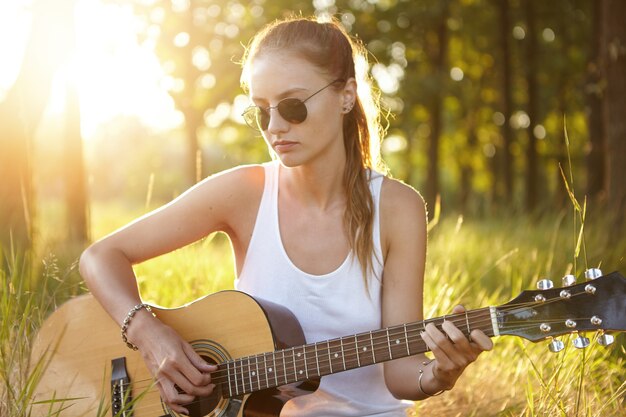 Mujer joven tocando la guitarra en la naturaleza durante la puesta de sol