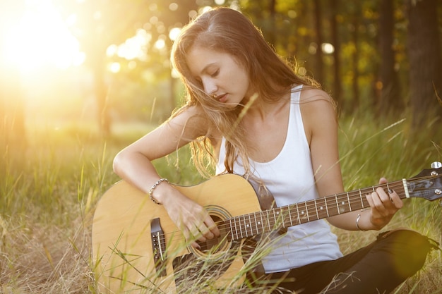 Mujer joven tocando la guitarra en la naturaleza durante la puesta de sol