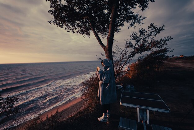 Mujer joven toma fotografías de la puesta de sol del mar por teléfono inteligente