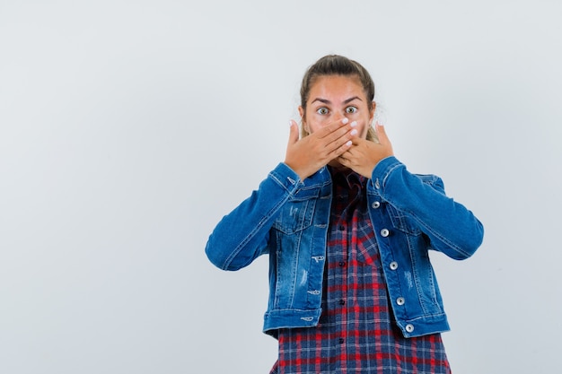 Foto gratuita mujer joven tomados de la mano en la boca en camisa, chaqueta y mirando asustado, vista frontal.