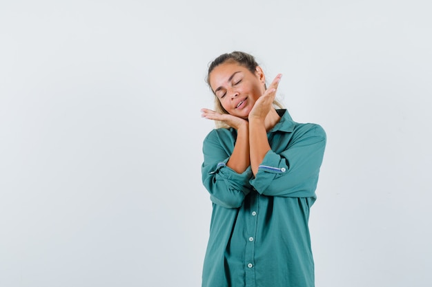 Mujer joven tomados de la mano debajo de la barbilla mientras cierra los ojos en blusa verde y parece feliz