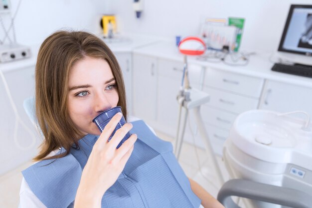 Mujer joven tomando agua mientras está sentado en la silla dental