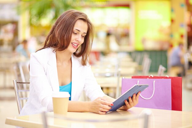 Mujer joven tomando un café y consultando la tableta