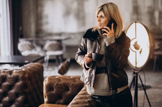 Mujer joven tomando café y hablando por teléfono en un café