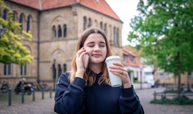 Una mujer joven tomando café y hablando por teléfono en un paseo por la ciudad