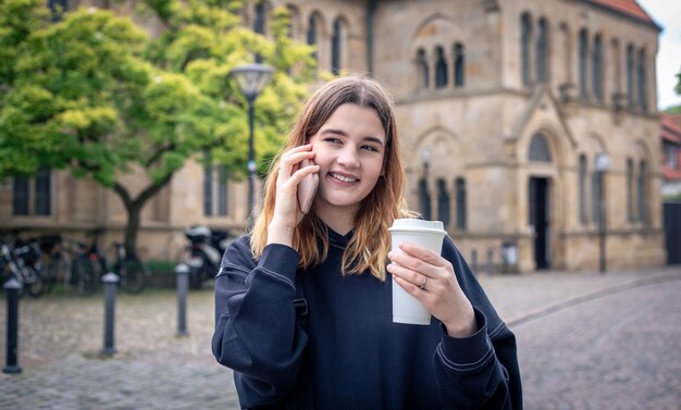 Una mujer joven tomando café y hablando por teléfono en un paseo por la ciudad