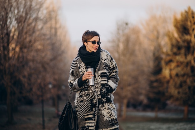 Mujer joven tomando café por la mañana y caminando en el parque