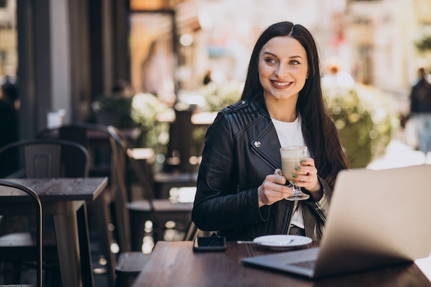 Mujer joven tomando café y trabajando en un portátil en un café