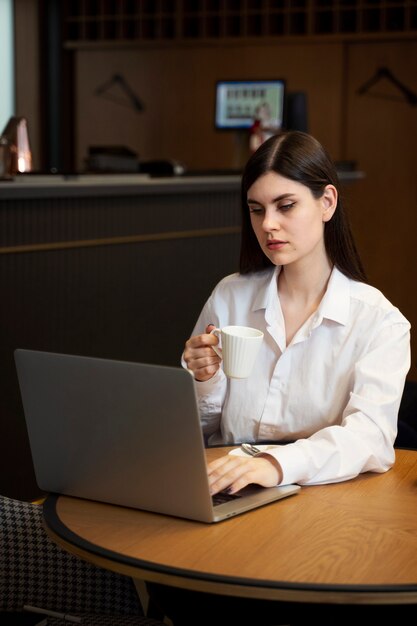 Mujer joven tomando café y trabajando en su computadora portátil en un restaurante