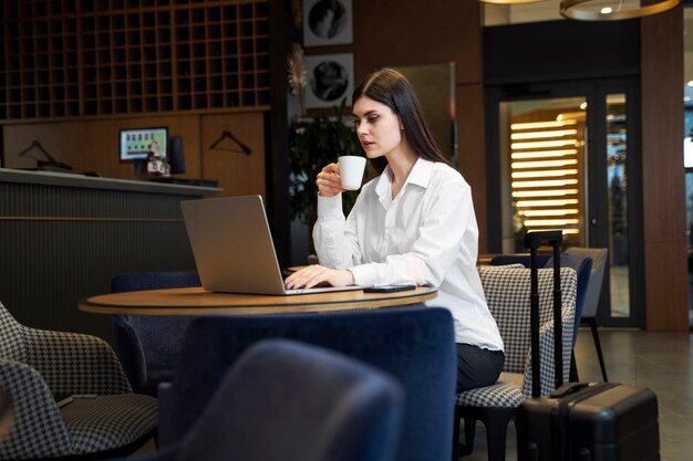 Mujer joven tomando café y trabajando en su computadora portátil en un restaurante