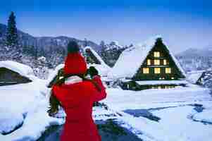 Foto gratuita mujer joven tomando una foto en la aldea de shirakawa-go en invierno, japón.