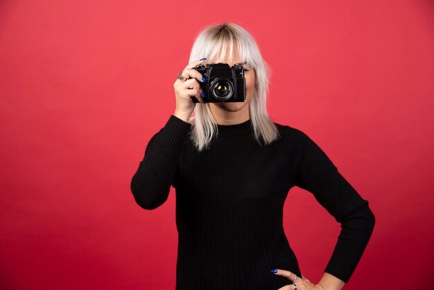 Mujer joven tomando fotografías con una cámara sobre un fondo rojo. Foto de alta calidad