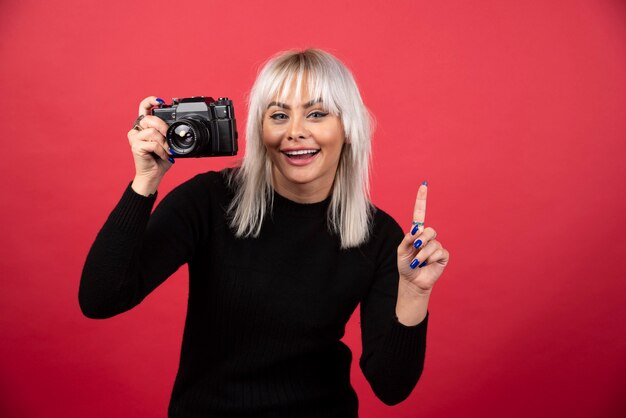 Mujer joven tomando fotografías con una cámara sobre un fondo rojo. Foto de alta calidad