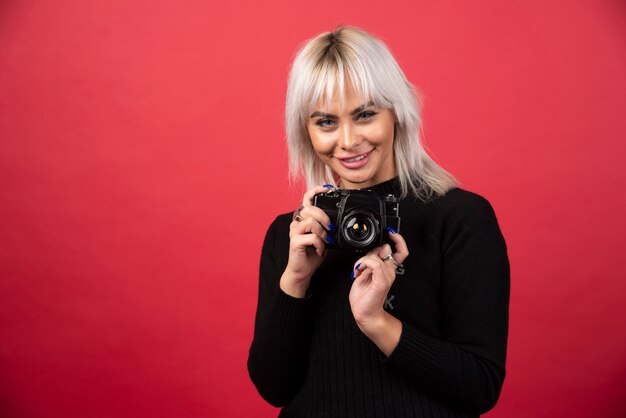 Mujer joven tomando fotografías con una cámara sobre un fondo rojo. Foto de alta calidad