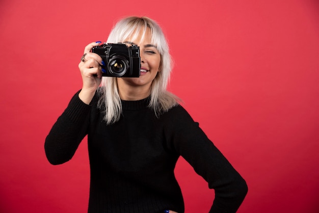 Mujer joven tomando fotografías con una cámara sobre un fondo rojo. Foto de alta calidad