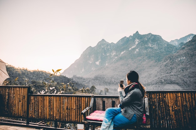 Mujer joven tomando fotos con su teléfono de la hermosa vista a la montaña