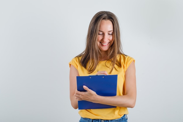 Mujer joven tomando notas en el portapapeles en camiseta, pantalones cortos y mirando ocupado