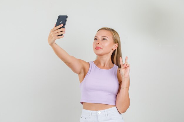 Mujer joven tomando selfie mostrando v-sign en camiseta