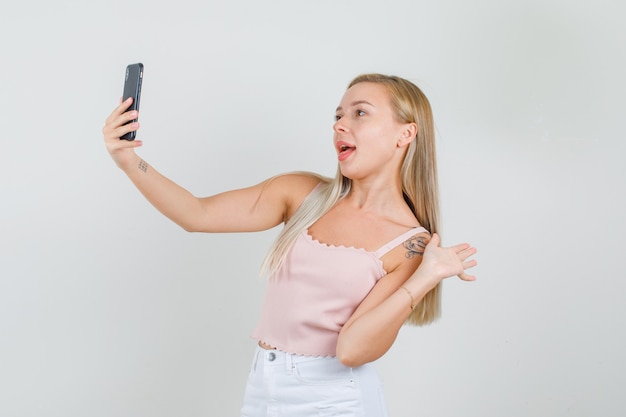 Mujer joven tomando selfie con signo de mano en camiseta, minifalda.