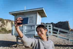 Foto gratuita mujer joven tomando un selfie con su teléfono inteligente en la playa