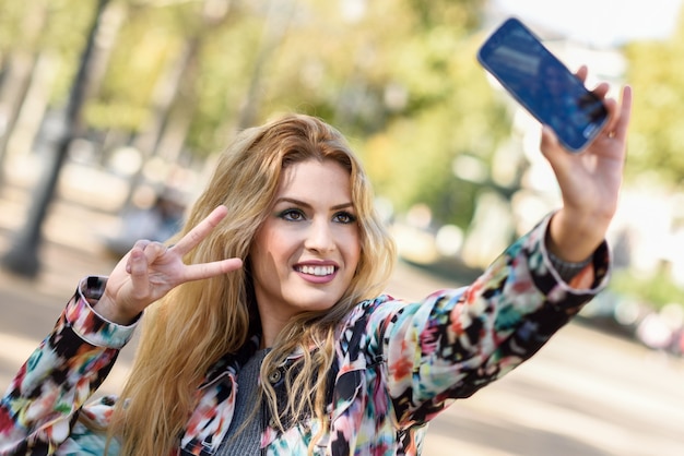 Mujer joven tomándose una autofoto y mostrando el gesto de la victoria