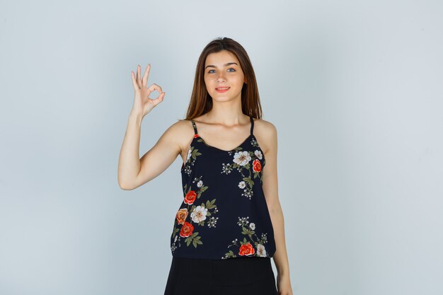 Mujer joven en top floral mostrando gesto ok y mirando complacido