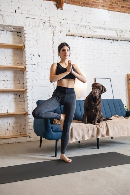 Mujer joven trabajando en casa durante el encierro, ejercicios de yoga con el perro