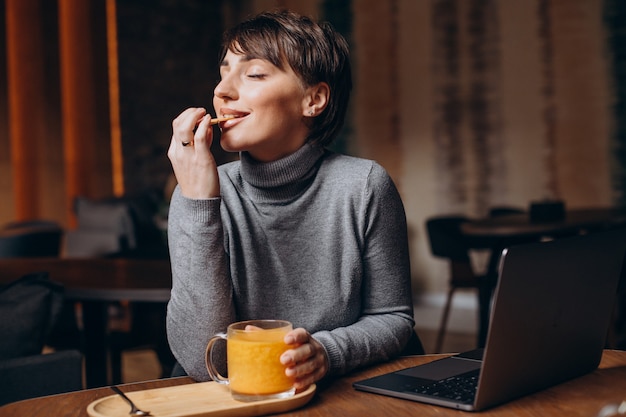 Mujer joven trabajando en la computadora y bebiendo té caliente
