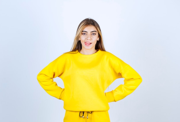 Mujer joven en traje amarillo posando para la cámara sobre la pared blanca