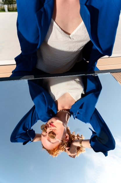 Mujer joven en traje azul posando con espejo al aire libre