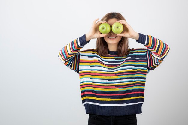 Mujer joven en traje casual con manzanas verdes delante de los ojos.