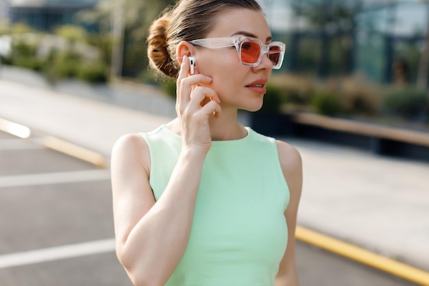 mujer joven en traje casual usando auriculares inalámbricos al aire libre