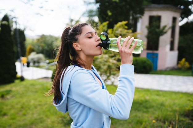 Mujer joven en traje deportivo bebe de una botella después de un entrenamiento