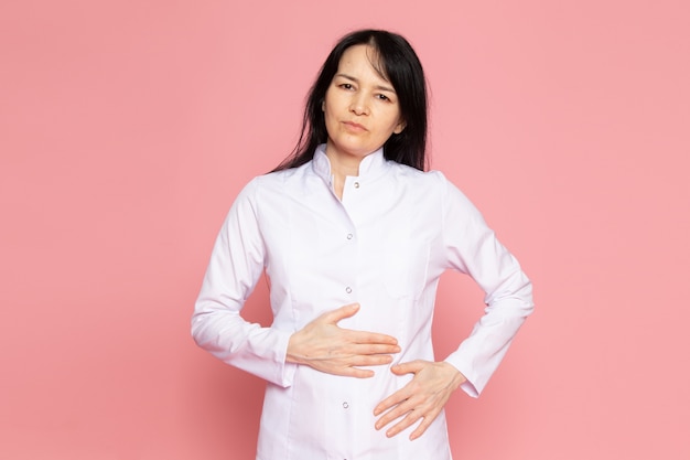 mujer joven en traje médico blanco con dolor de estómago en rosa