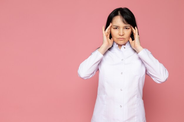 mujer joven en traje médico blanco con un fuerte dolor de cabeza en rosa