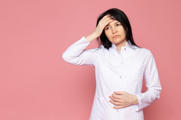 mujer joven en traje médico blanco con un fuerte dolor de cabeza en rosa